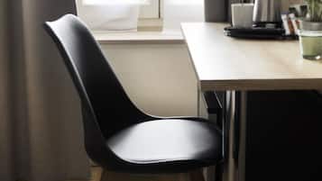 A modern dining area with a wooden table and two black chairs. A coffee maker and a potted plant are on the table.