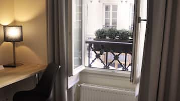 Habitación de hotel con cama, escritorio con lámpara, silla, ventana con vistas a edificios y radiador.