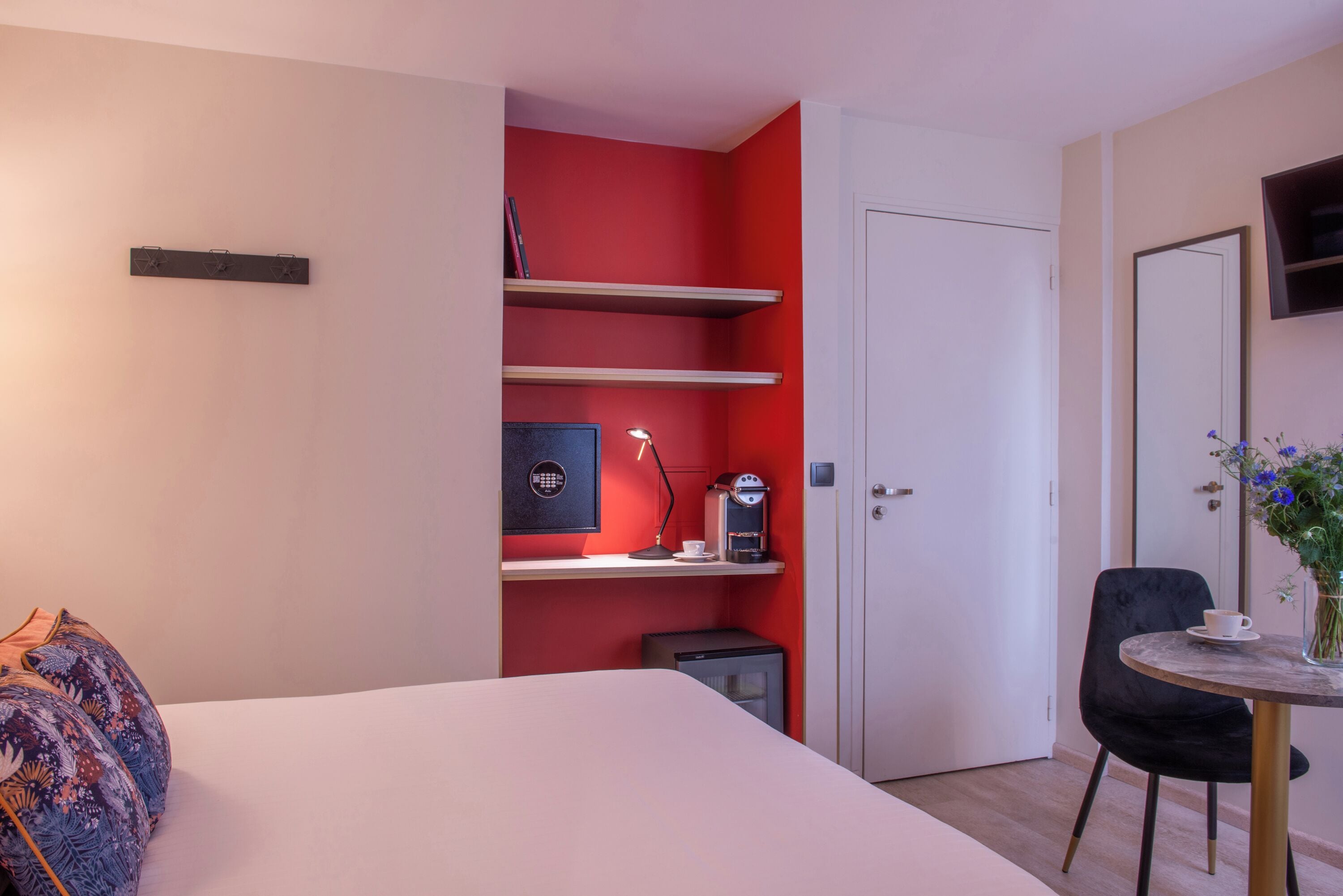 A hotel room with a bed, a desk with a lamp, a coffee machine, and a small cabinet.