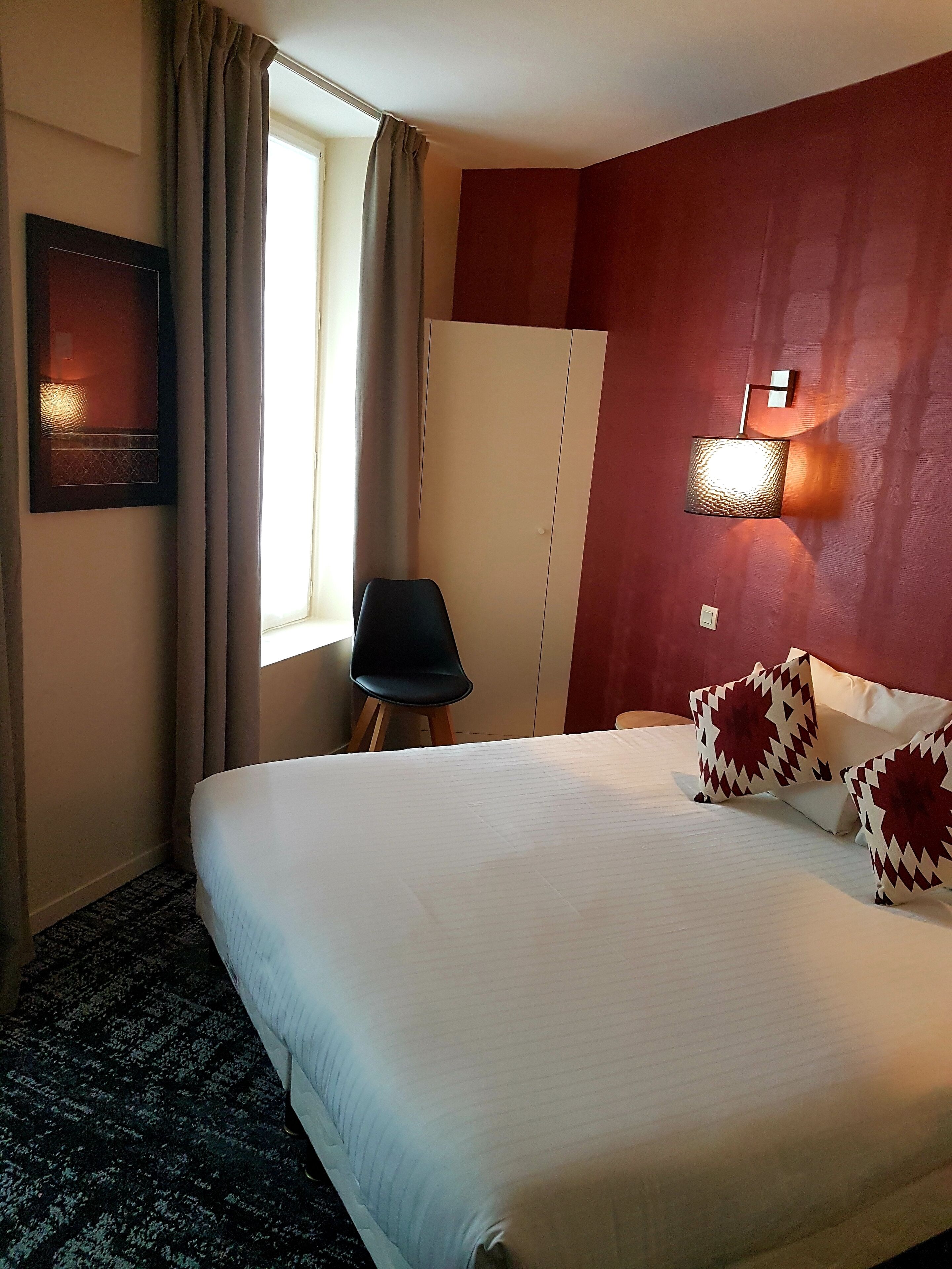 Ein Hotelzimmer mit einem großen Bett, einem Sessel, einem Kleiderschrank und einer Wandleuchte.