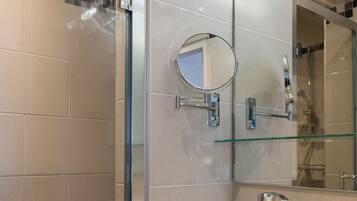 Een moderne badkamer met een douchecabine van glas, een witte wastafel, een spiegel en een glazen plank.