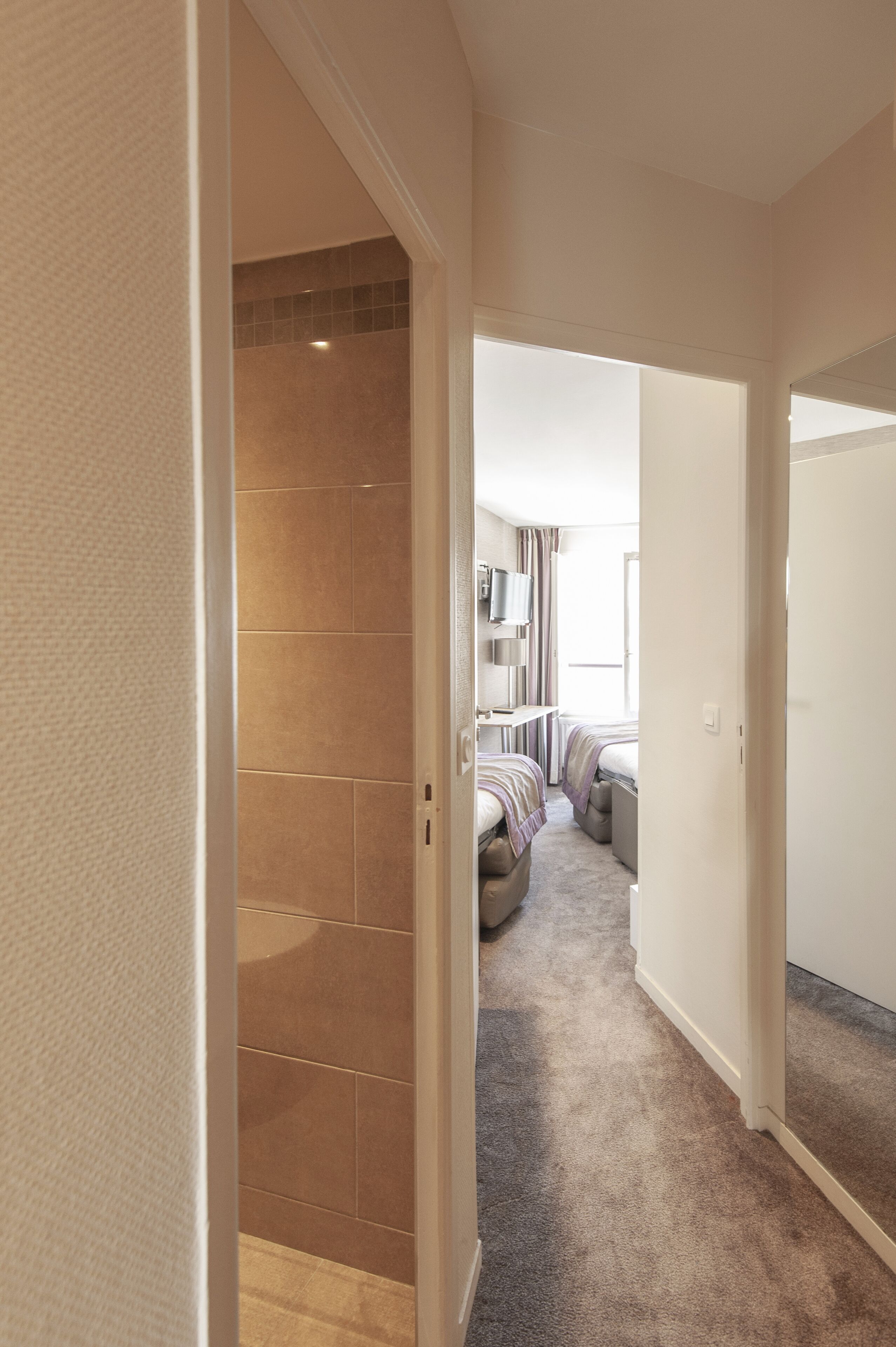 Un couloir menant à une chambre dotée d’une douche, d’un lit et d’un téléviseur.
