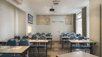 Un salón de conferencias con mesas, sillas, un proyector y una pared de piedra.
