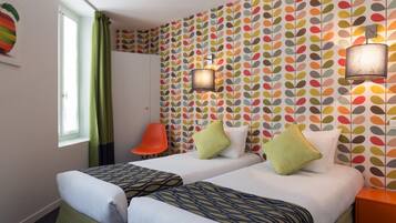 Een hotelkamer met twee bedden, een raam met gordijnen, een stoel en een behang met patroon.
