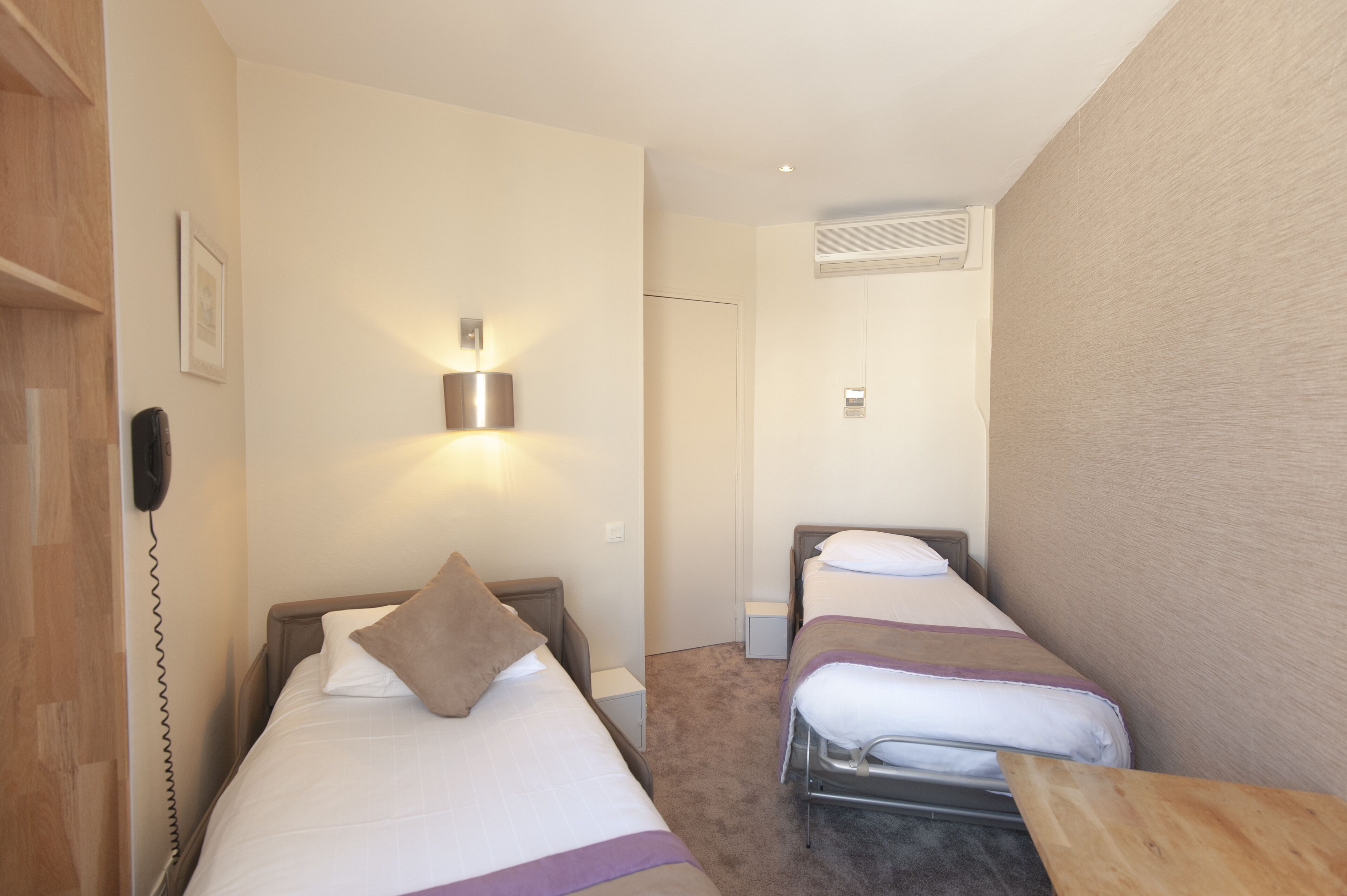 Une chambre d’hôtel avec deux lits simples, une table de chevet, une lampe et un téléphone fixé au mur.
