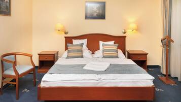 A neatly made bed with white linens and striped pillows, flanked by two bedside tables with lamps, a wooden chair, and a framed picture on the wall.