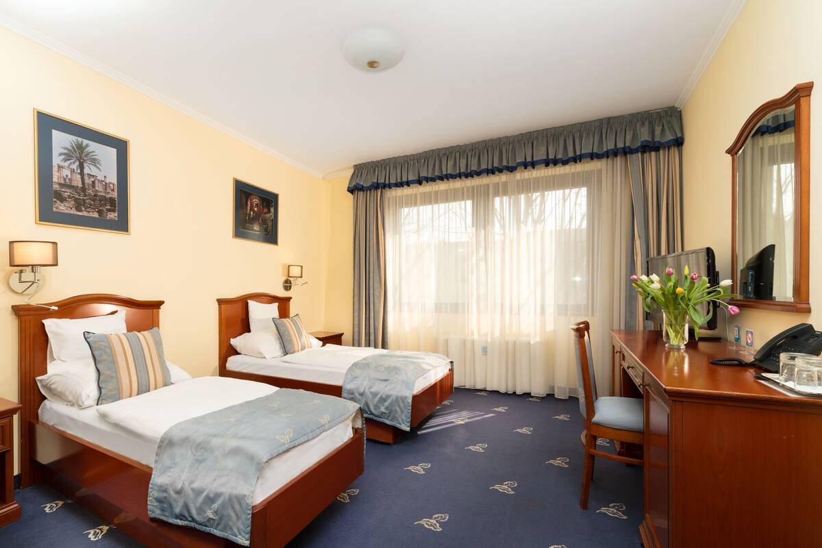 Habitación de hotel con dos camas, un escritorio con una silla, un espejo y un florero con flores.