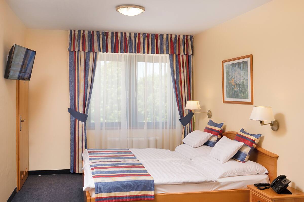 Una habitación de hotel con cama, lámparas de noche, teléfono y un cuadro en la pared.