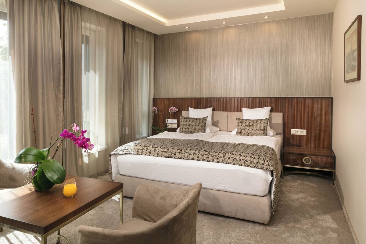 Una habitación de hotel moderna con una cama grande, una mesita de noche de madera, un escritorio con una silla y un florero con flores.