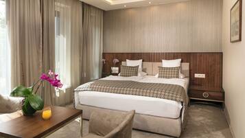 Una habitación de hotel moderna con una cama grande, una mesita de noche de madera, un escritorio con una silla y un florero con flores.