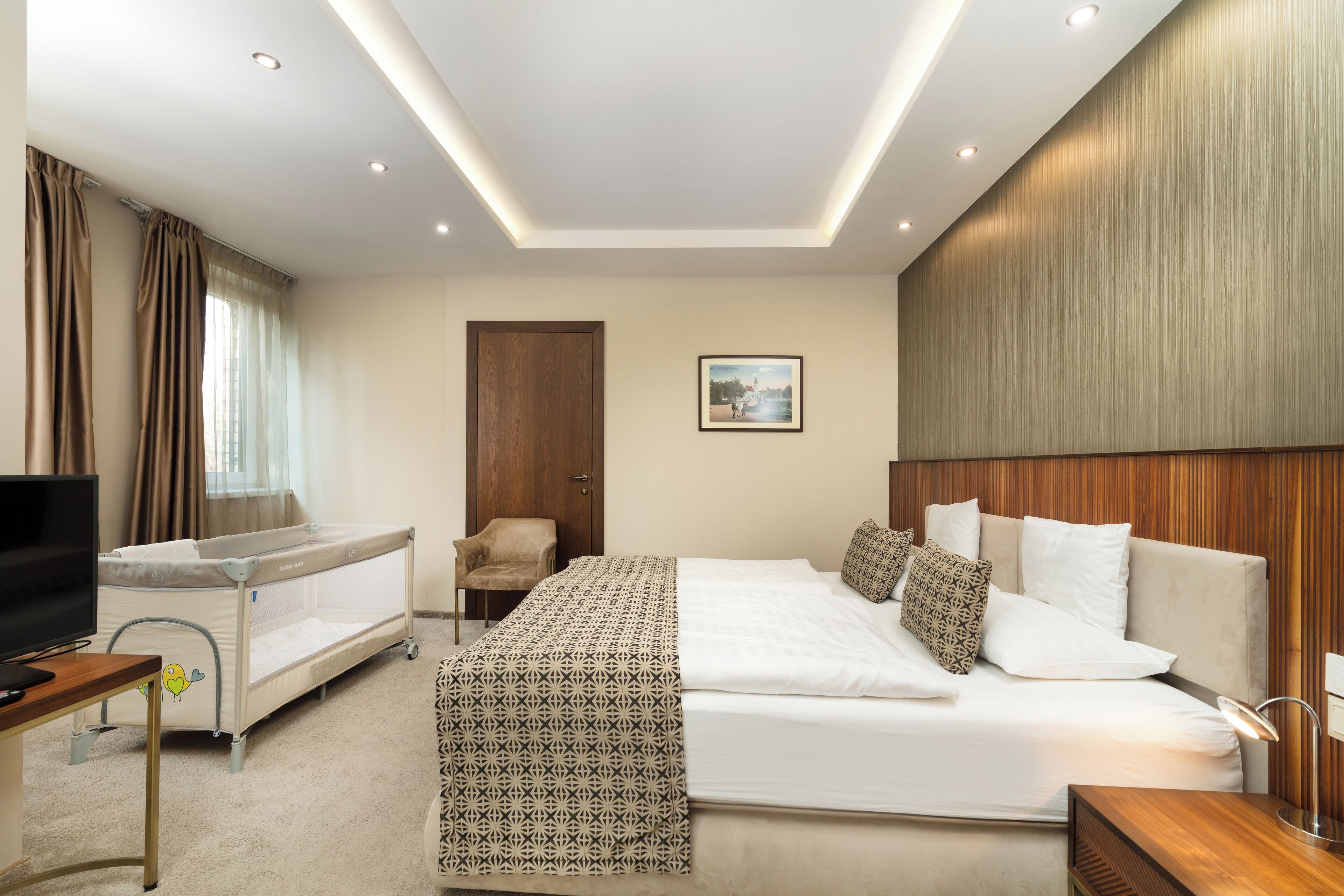 A hotel room with a large bed, a baby crib, a television, and a desk.