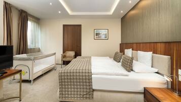 A hotel room with a large bed, a baby crib, a television, and a desk.