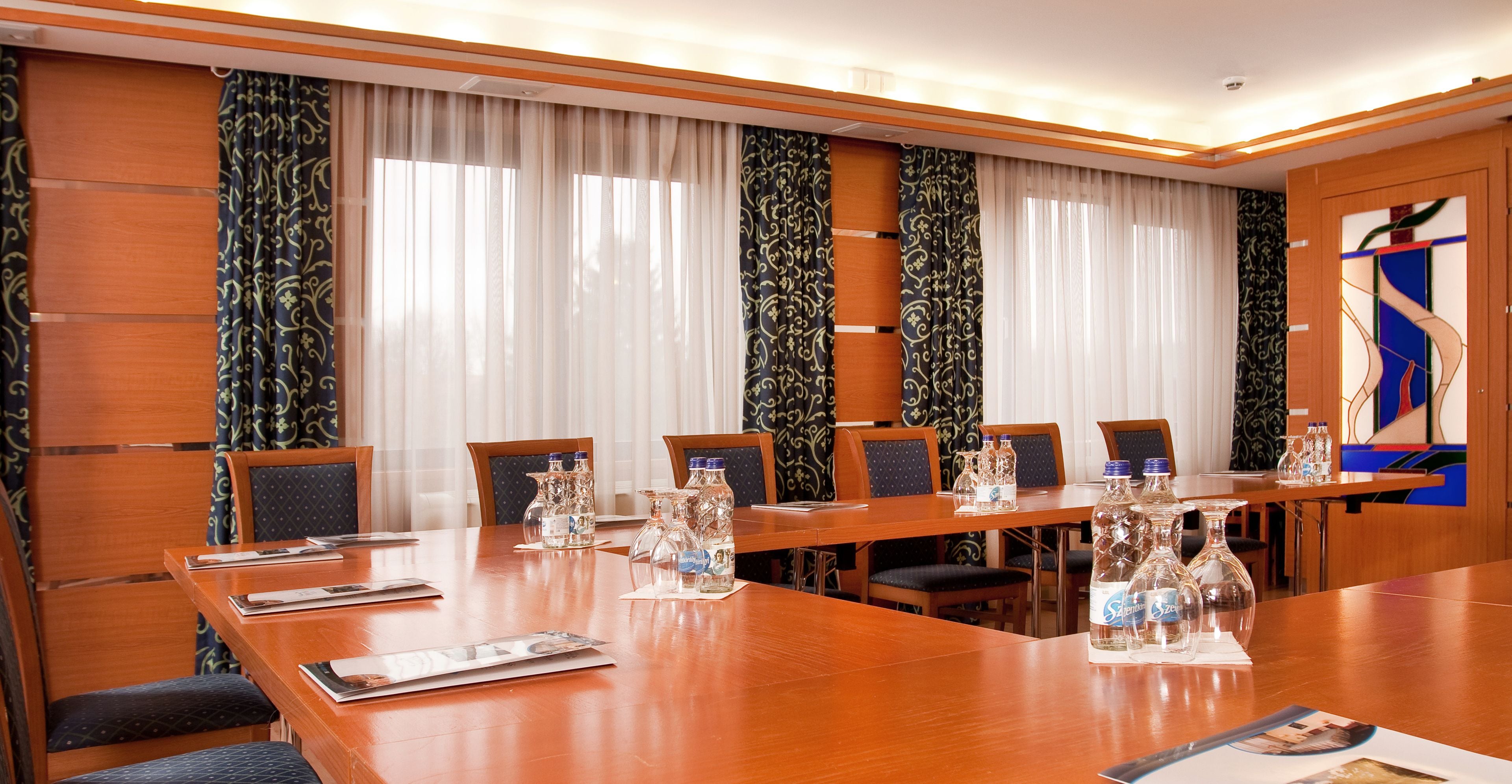 A conference room with a long wooden table, six chairs, and water bottles on the table.