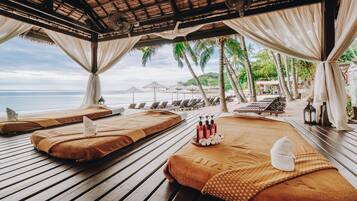 A beachside spa area with wooden loungers, towels, and bottles of lotion.