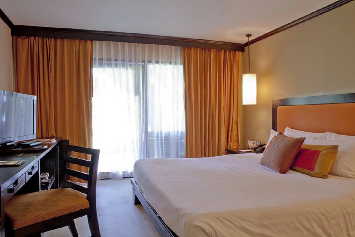 A hotel room with a bed, a desk with a chair, a television, and curtains.