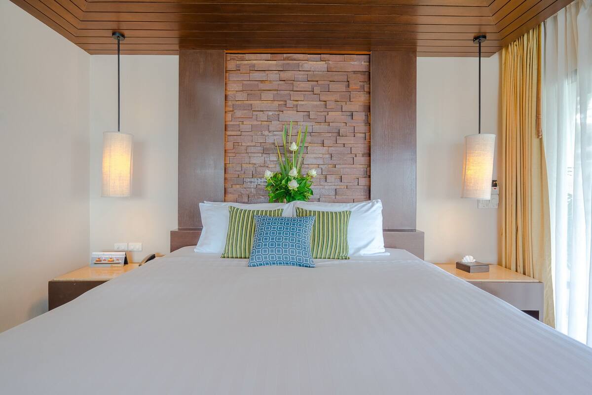 A hotel room with a large bed, a brick accent wall, and a bedside table with a lamp.