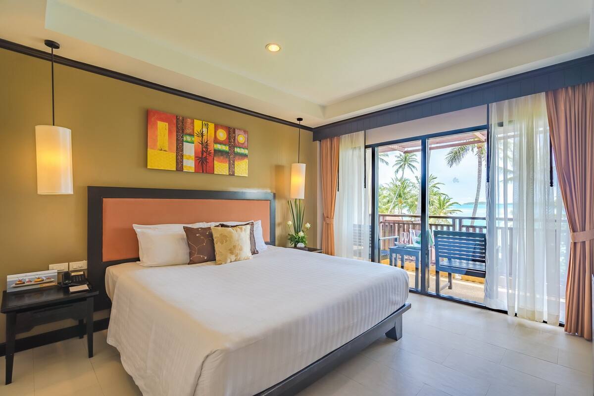A hotel room with a large bed, a nightstand, a painting on the wall, and a view of the outdoors.