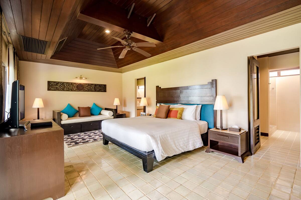 A hotel room with a large bed, a sofa, a desk, and a ceiling fan.