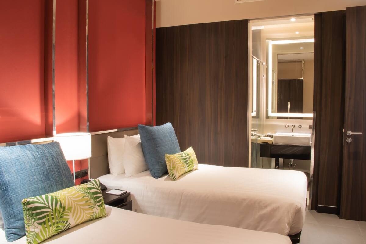 A hotel room with two beds, a large mirror, a bathroom with a sink and mirror, and red and brown walls.