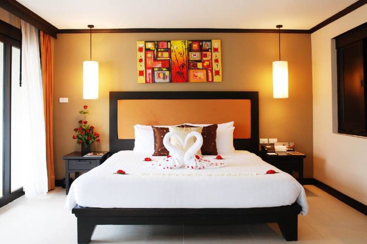 A hotel room with a large bed, two bedside tables, a wall-mounted artwork, and a window with curtains.