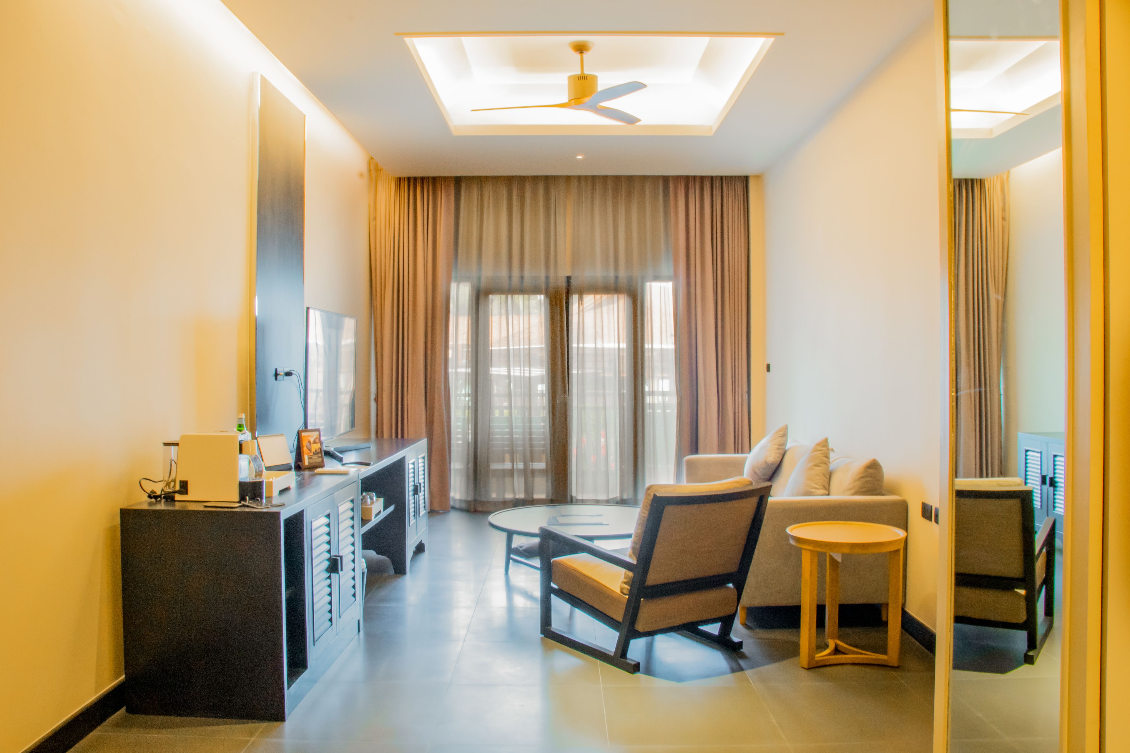 Une chambre d’hôtel moderne dotée d’un coin salon, d’un bureau et d’une grande fenêtre avec des rideaux.