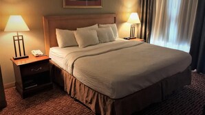 A hotel room with a large bed, two bedside lamps, a nightstand with a phone, and a framed picture on the wall. - Host Inn All Suites (Wilkes-Barre)