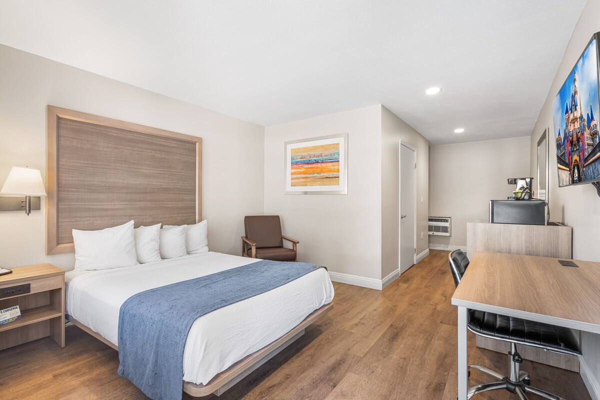 A hotel room with a bed, a desk, a chair, a lamp, and a painting on the wall.