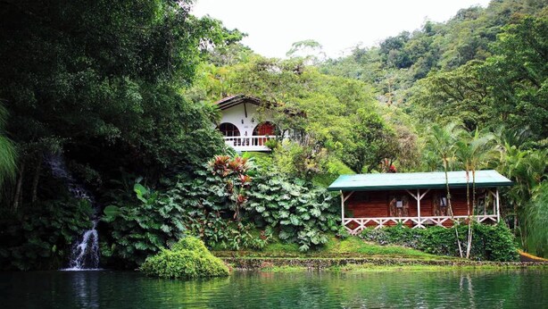 A house with a balcony overlooking a lush garden and a waterfall. - Rio Perlas Thermal Resort & Spa (Dulce Nombre)