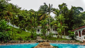 A pool with a rock centerpiece, surrounded by lush greenery and a white building with arched windows. - Rio Perlas Thermal Resort & Spa (Dulce Nombre)