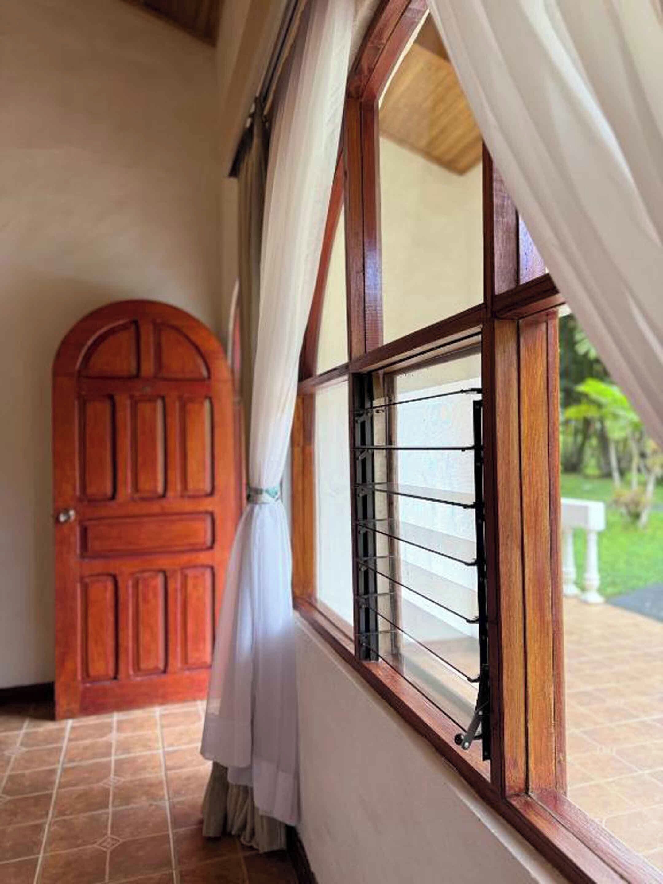 A wooden door with a window, white curtains, and a tiled floor.