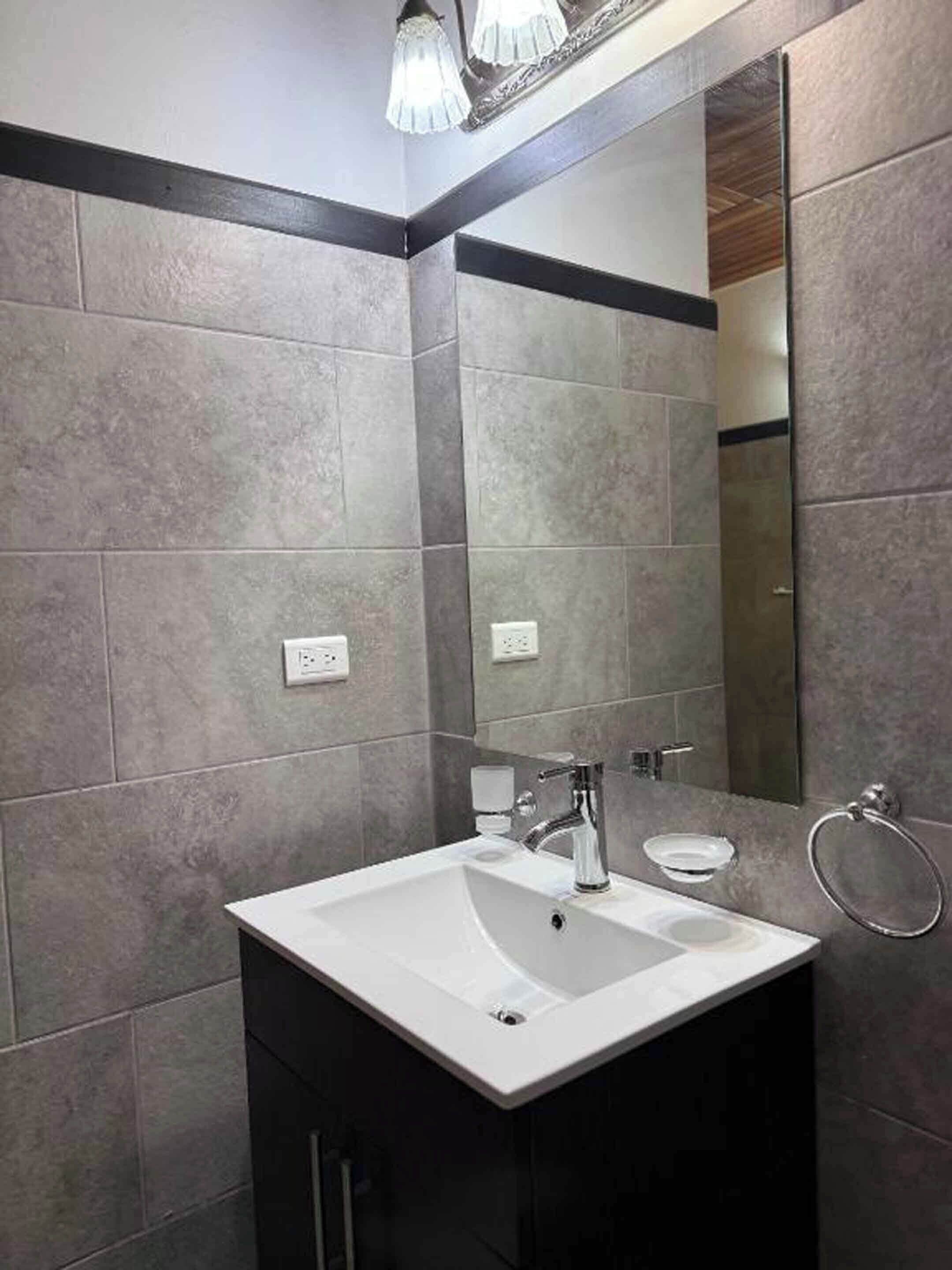 Een moderne badkamer met grijze betegelde wanden, een wit wastafelmeubel en een grote spiegel.