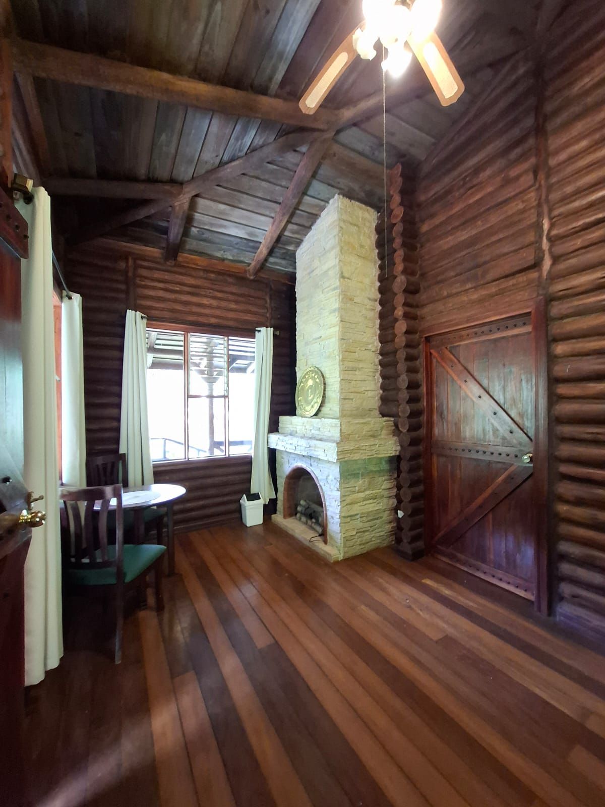 A log cabin interior with a stone fireplace, wooden flooring, and a ceiling fan.