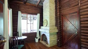 A log cabin interior with a stone fireplace, wooden flooring, and a ceiling fan.