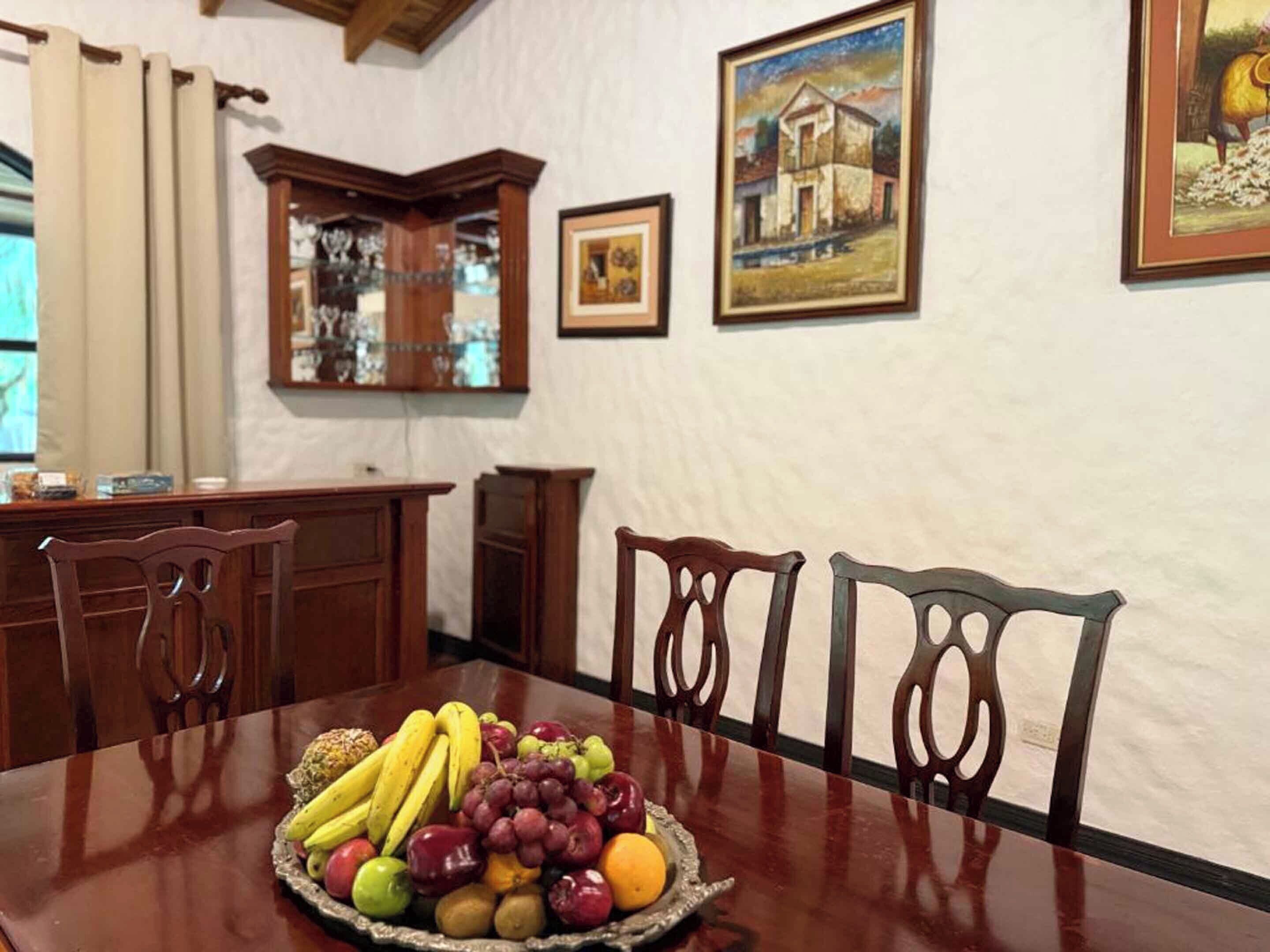 Un comedor con una mesa de madera dispuesta con fruta, rodeado de sillas de madera.