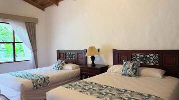 Una habitación de hotel con dos camas, una ventana con cortinas, techo de madera y una mesita de noche con lámpara.