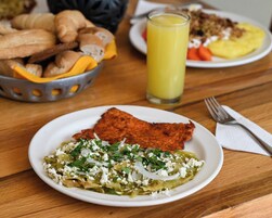 Una mesa de comedor con un plato de enchiladas, un vaso de jugo de naranja y una cesta de pan.