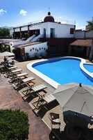 Una piscina con sillas de descanso y sombrillas, un edificio con cúpula roja y un cielo azul despejado.