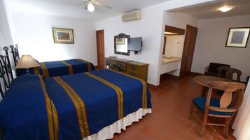 A hotel room with two beds, a desk, a chair, a ceiling fan, and a television.