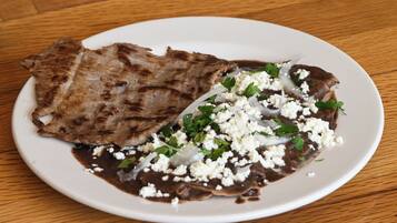 A plate with grilled meat and a sauce, garnished with herbs and crumbled cheese.