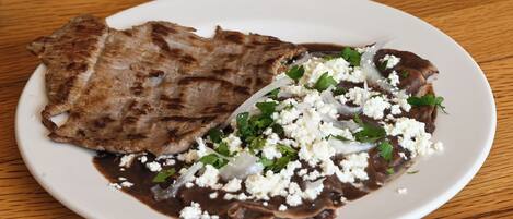 A plate with grilled meat and a sauce, garnished with herbs and crumbled cheese.
