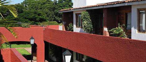 Un patio con un muro rojo, un edificio blanco y un farol negro.