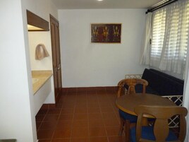 Un pequeño comedor con una mesa y sillas de madera, un cuadro colgado en la pared y una ventana con cortinas.