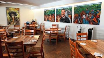 A dining area with wooden tables and chairs, artwork on the walls, and a camera on a tripod.