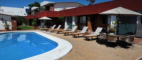 A pool area with lounge chairs and umbrellas, surrounded by buildings with red roofs and white walls.