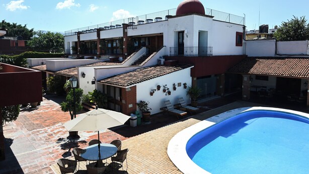 Un área de piscina en la azotea con piscina, mobiliario exterior y un edificio con cúpula roja y cruz en la parte superior.