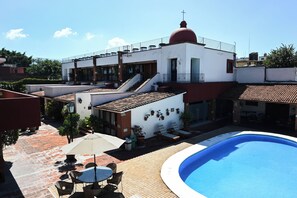 A rooftop pool area with a swimming pool, outdoor seating, and a building with a red dome and a cross on top. - Hotel Hacienda (Oaxaca)