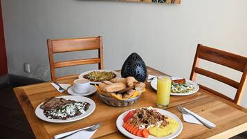 Una mesa de madera con platos de comida, sillas y un cuadro en la pared.