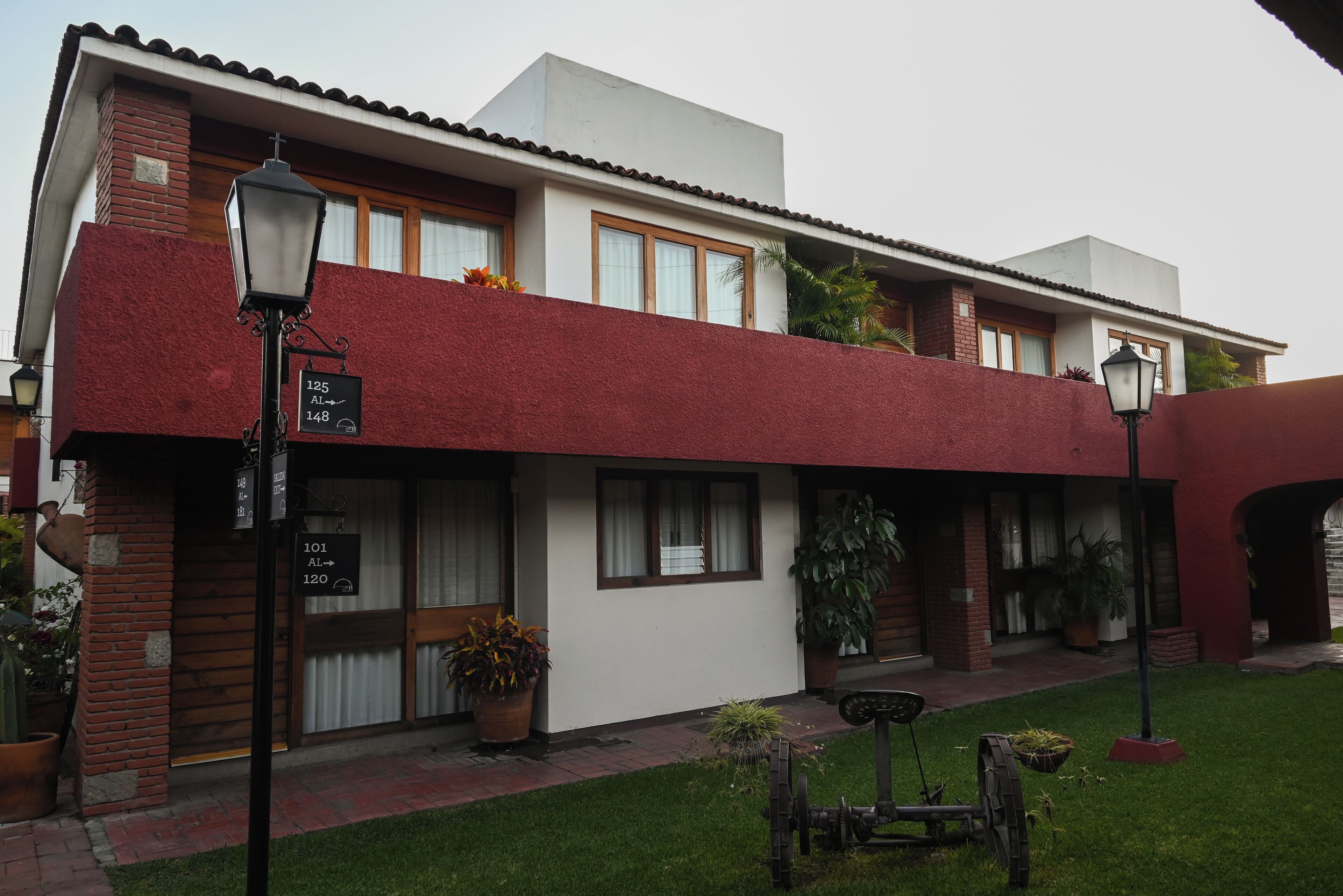 A two-story building with a red facade, multiple windows, and potted plants.