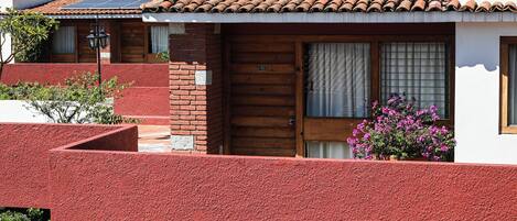A two-story building with a red exterior, a wooden door, and a window with curtains.