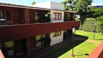 A two-story building with a red exterior, multiple windows, and a small garden area with a lawn and a few potted plants.